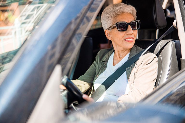Joyful senior lady in sunglasses driving car