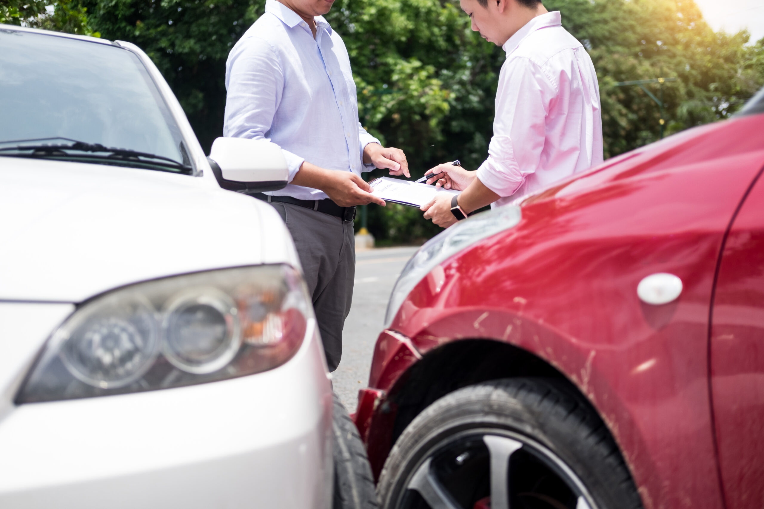 An insurance agent writing on a clipboard while examining car after an accident.