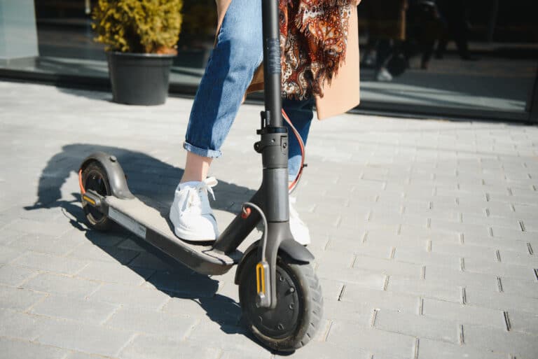 Photo of a person riding an electric scooter on the sidewalk.